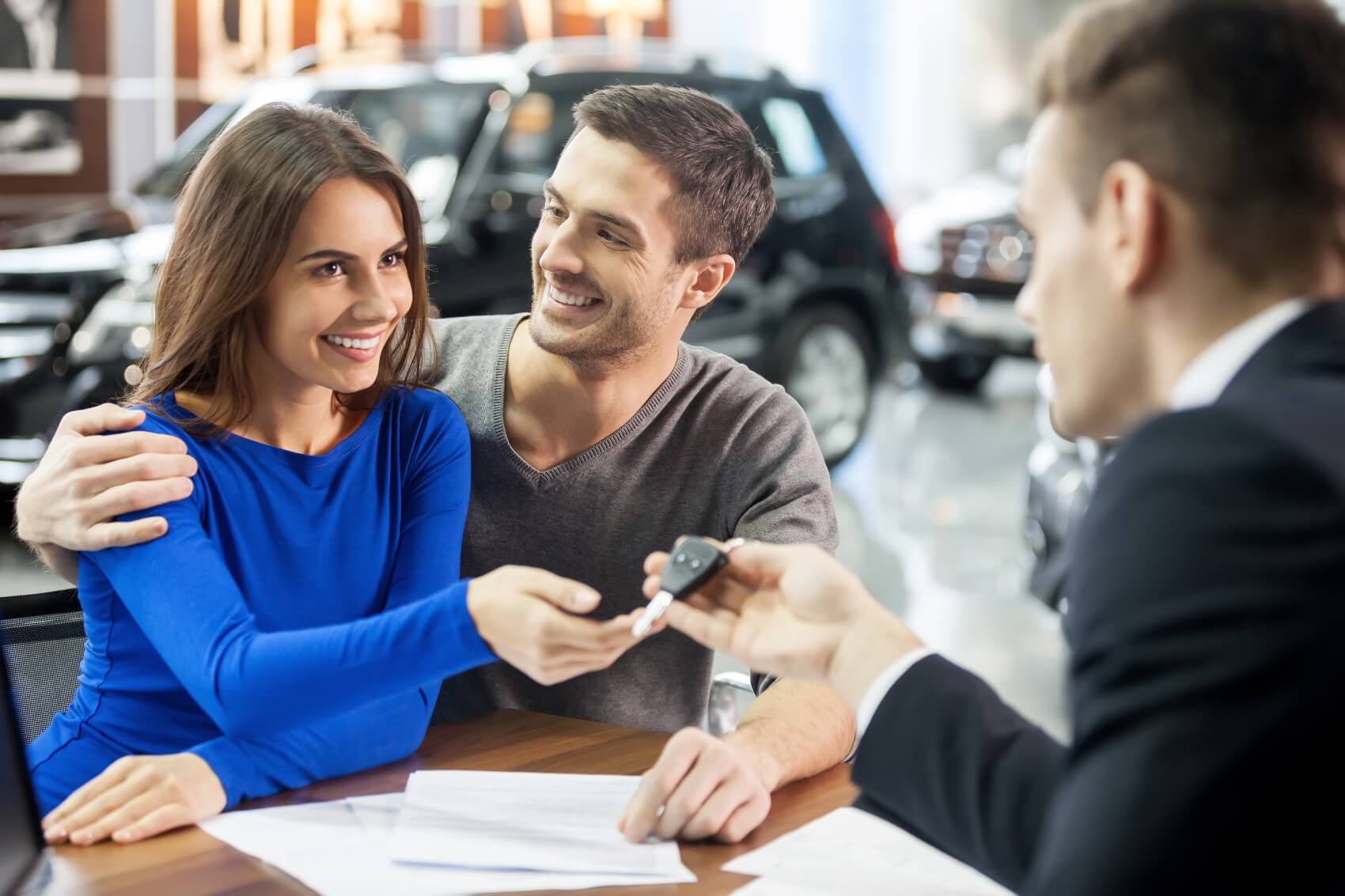 sales manager giving keys to couple in dealer showroom